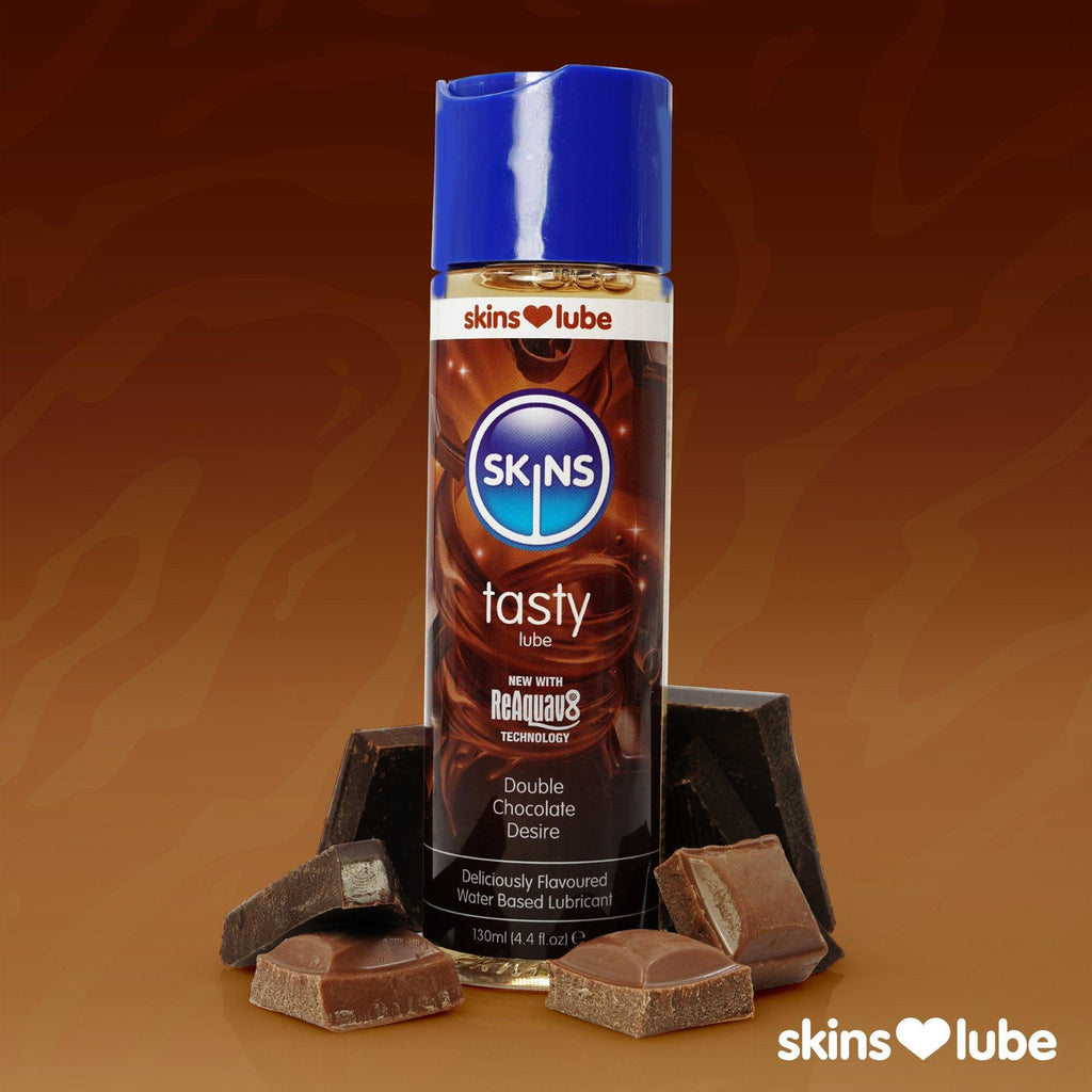 A brown gradient background with a Skins Double Chocolate Lube stood in the middle surrounded by pieces of chocolate