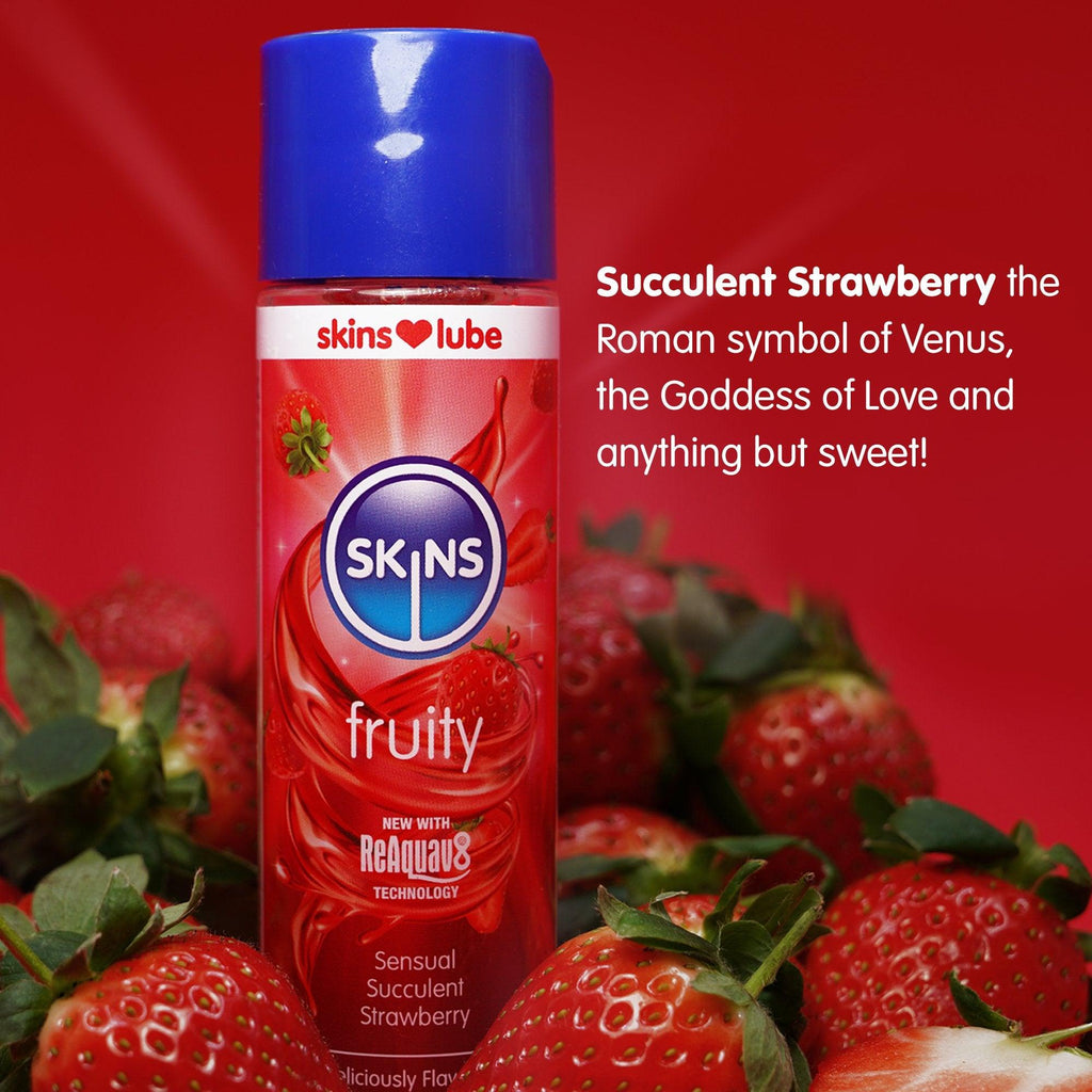 Red background with real strawberries at the bottom and a Skins strawberry lube standing in the middle. The lube is in focus where as the strawberries are slightly out of focus. Next to the bottle of lube is some text about the strawberry flavour.