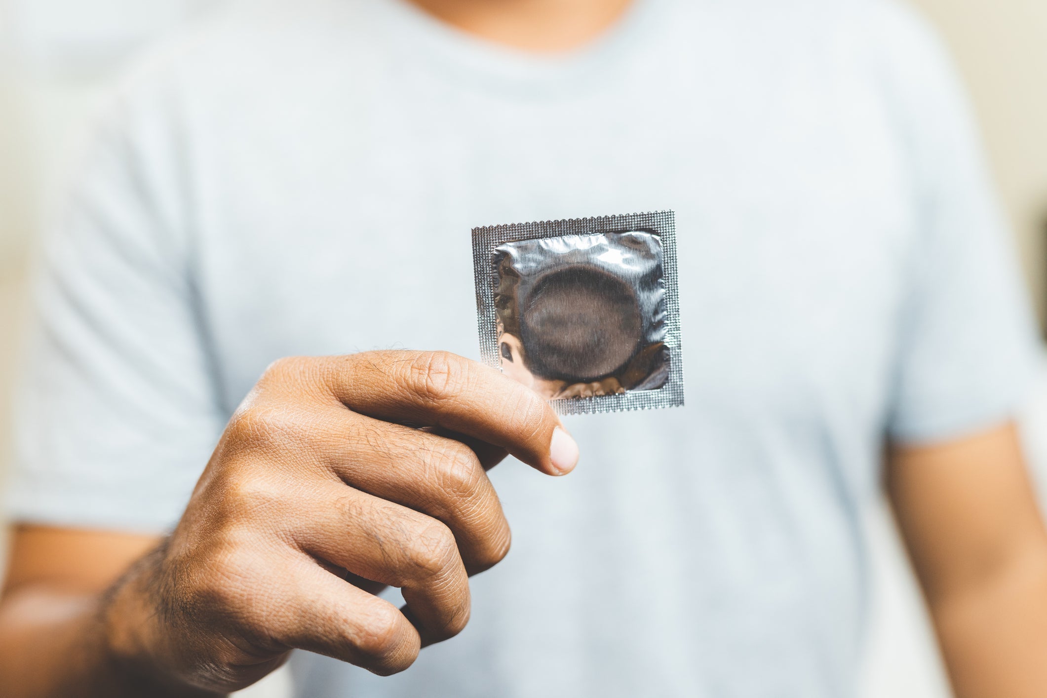 man in a grey t-shirt holding a condom wrapper 