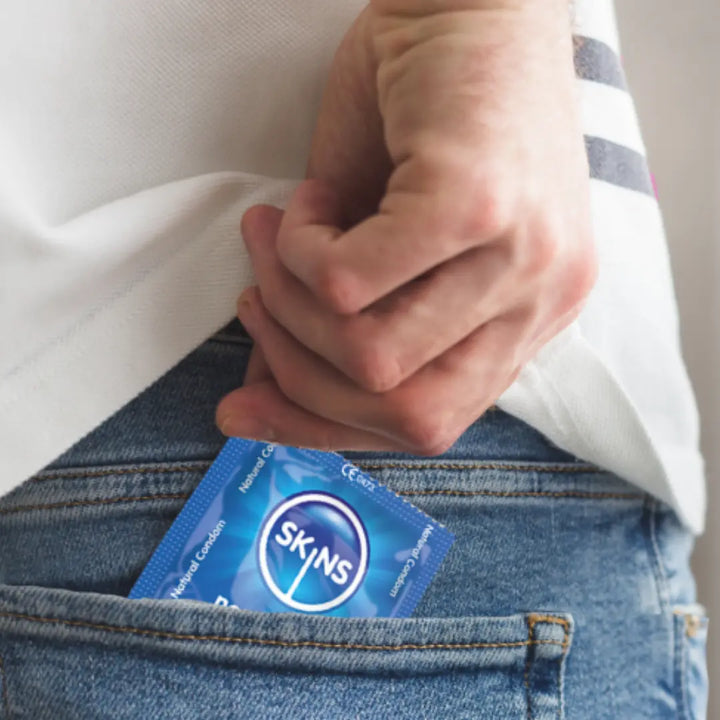 Person placing a Skins branded condom packet into their jeans pocket.