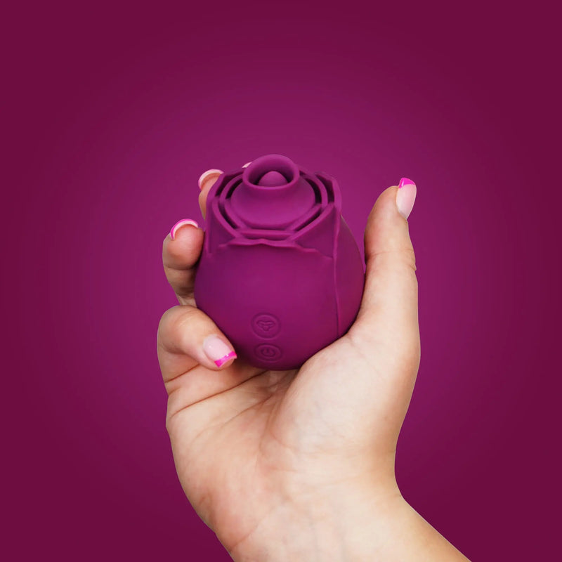 womans hand holding the Flutterz rose sex toy on a purple background