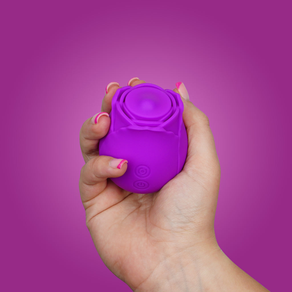 A woman's hand holding the Twirl rose clitoral vibrator on a purple background