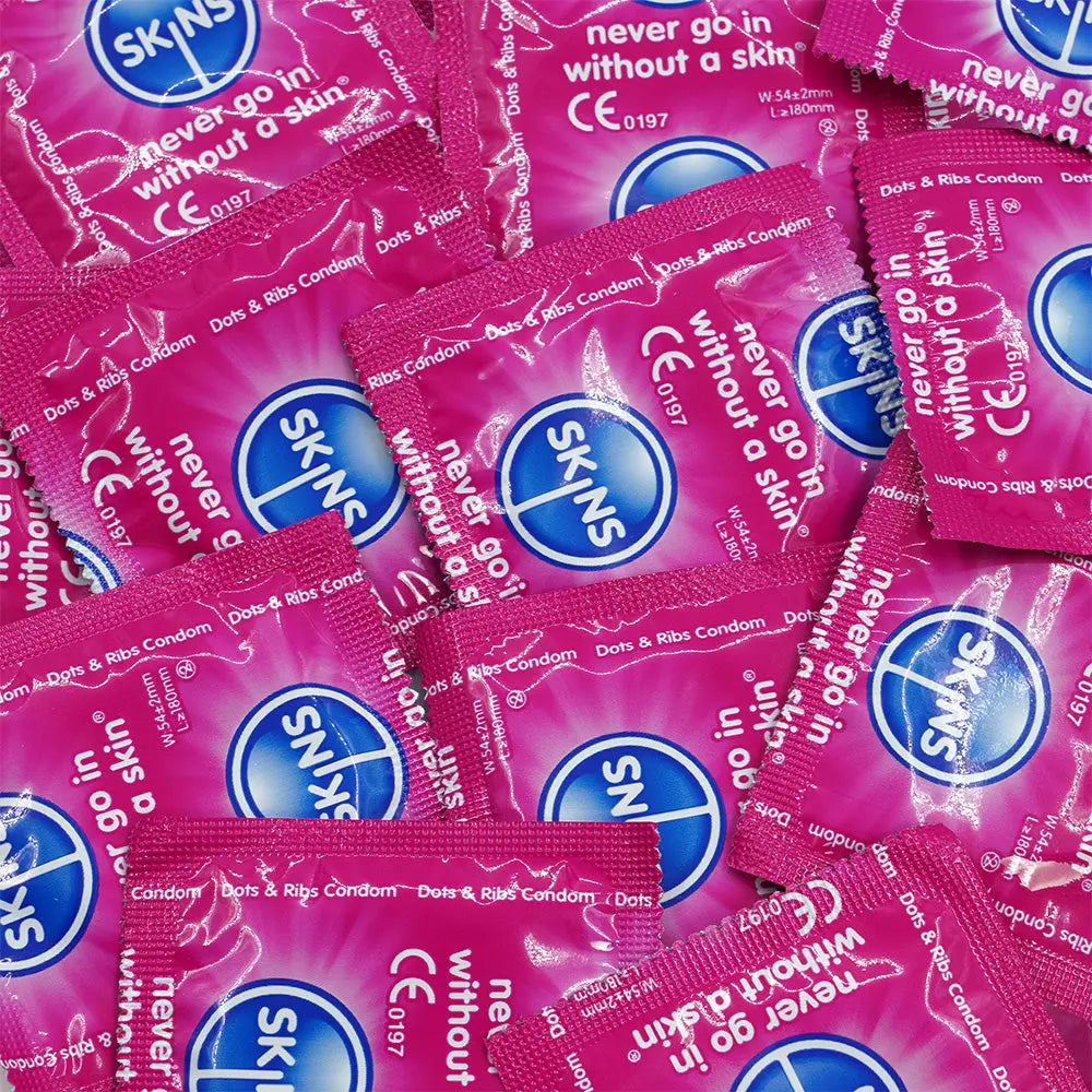 Multiple packs of Skins condoms on a pink background