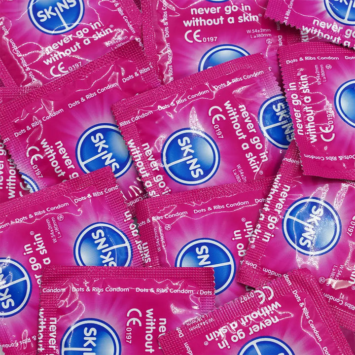 Multiple packs of Skins condoms on a pink background