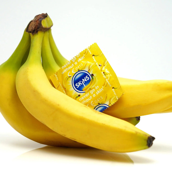 A white background with a bunch of bananas and a Skins Banana condoms foil on the bananas.