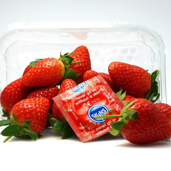 A white background with a punnet of strawberries amongt a Skins Strawberry condom foil