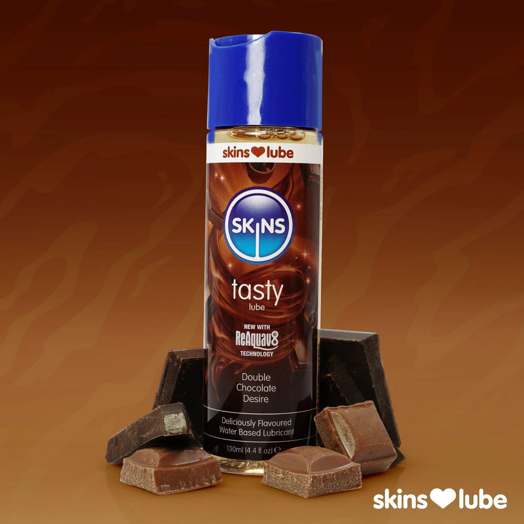 A brown gradient background with a Skins Double Chocolate Lube stood in the middle surrounded by pieces of chocolate