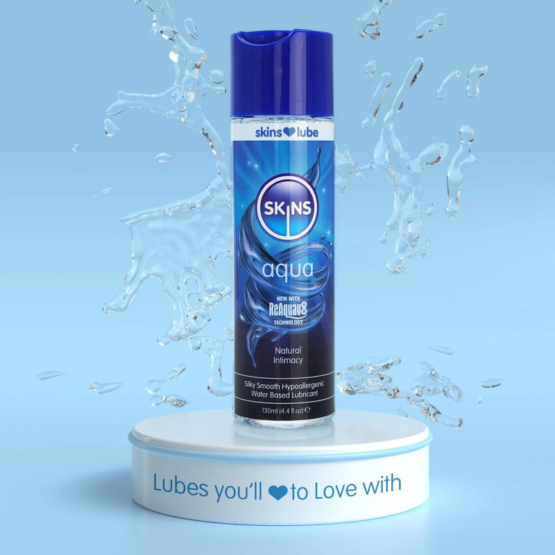 A pale blue background with a water splash in the middle. In front of this a Skins Aqua Lube 130ml stood on a short, circular platform.