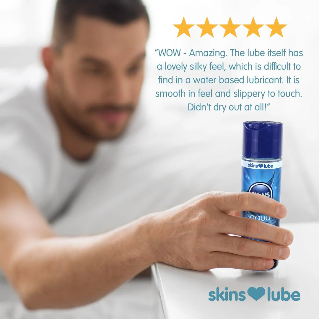 A man in the background, slightly burred reaching out for the Skins Aqua Lube bottle which is in the forefront of the image. Above the bottle of lube a 5 star review.